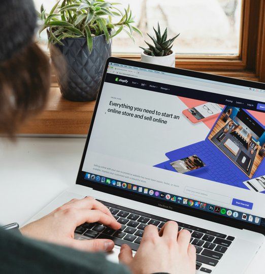 person using macbook pro on white table with shopify on it
