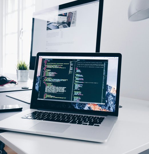 A MacBook with lines of code on its screen on a busy desk